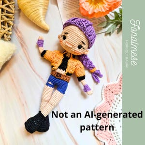 Puede incluir: Muñeca de ganchillo hecha a mano con un gorro morado y una trenza larga, que lleva una chaqueta naranja, pantalones cortos azules y zapatos negros. La muñeca tiene una cara sonriente. El texto de la imagen dice "Not an AI-generated pattern."