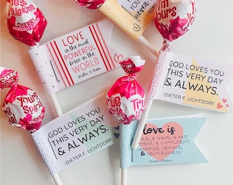 May include: An assortment of wrapped cherry-flavored lollipops and decorative flags with inspirational quotes. The flags feature quotes about love and faith, with a color palette of pink, white, and pastel hues.