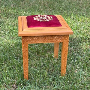 May include: A wooden stool with intricate carvings and a red velvet cushion with a gold geometric pattern.