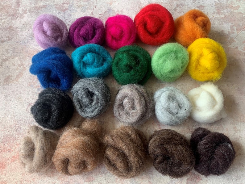 May include: Twenty-four balls of wool in various colors, including purple, pink, red, orange, yellow, green, blue, gray, brown, and white. The balls are arranged in rows on a light gray surface.