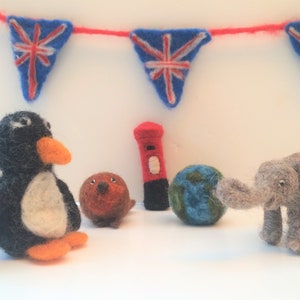 May include: A felt penguin, a felt elephant, a felt globe, a felt red mailbox, and a felt brown animal with a red nose. The background is a white wall with a red and blue bunting.