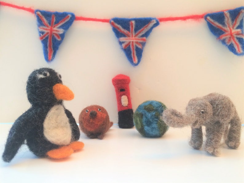 May include: A felt penguin, a felt elephant, a felt globe, a felt red mailbox, and a felt brown animal with a red nose. The background is a white wall with a red and blue bunting.