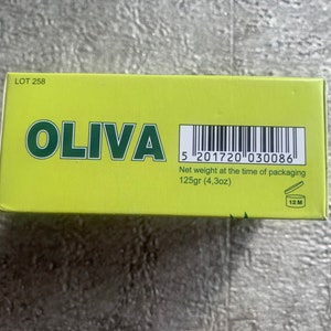 May include: A yellow box with the word "OLIVA" in green letters. The box has a barcode and the text "Net weight at the time of packaging 125gr (4,3oz)". There is also a symbol of an open jar with the text "12 M" inside.