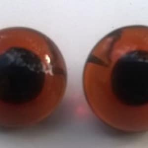 May include: Two orange plastic googly eyes with black pupils. The eyes are round and have a glossy finish.