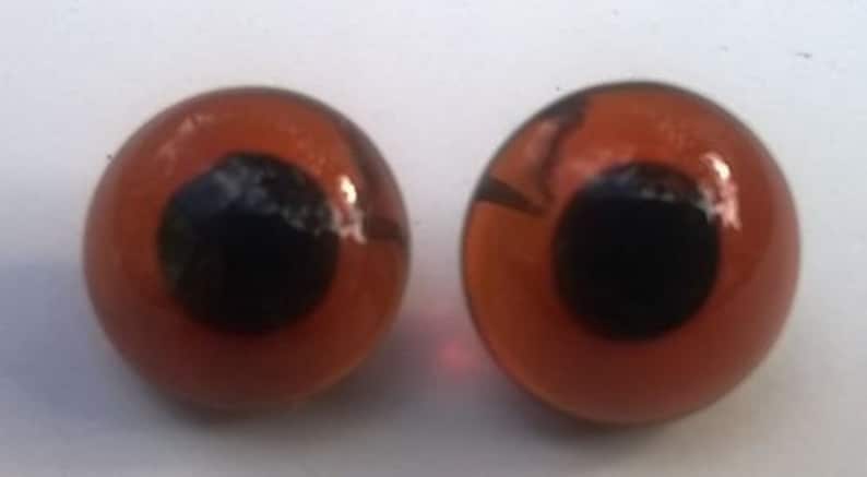 May include: Two orange plastic googly eyes with black pupils. The eyes are round and have a glossy finish.