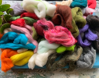 May include: A variety of colorful wool roving in different shades of green, blue, pink, red, orange, yellow, brown, white, gray, and purple. The wool is arranged in a pile on a blue surface.