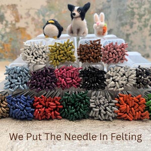 May include: A selection of felting needles in various colours, displayed in clear plastic containers. The image features felted animal figures: a penguin, a dog, and a rabbit. The text at the bottom reads, "We Put The Needle In Felting."