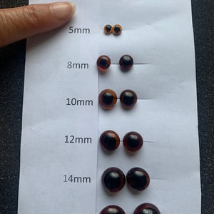 May include: A set of brown plastic safety eyes for crafts, ranging in size from 4mm to 16mm. The eyes are arranged in rows on a white background, with the size of each eye labelled in millimetres.