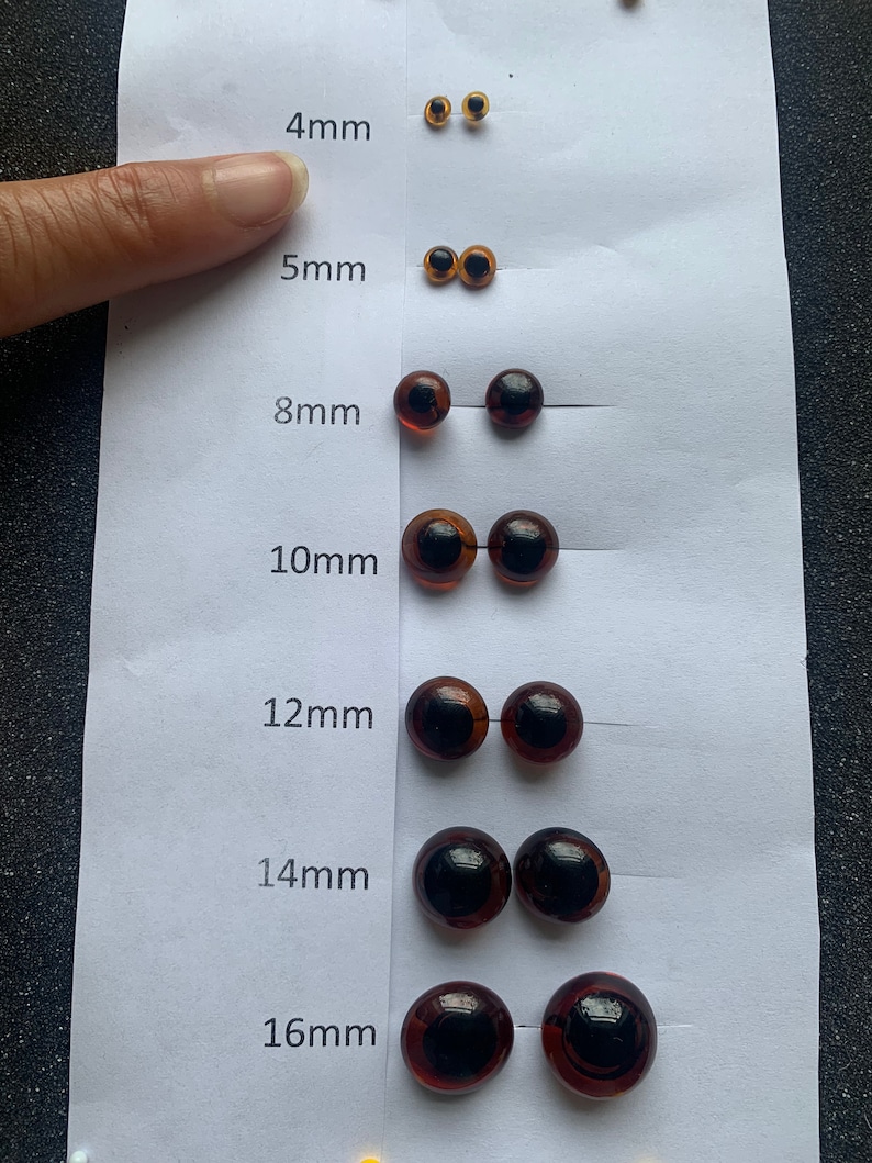 May include: A set of brown plastic safety eyes for crafts, ranging in size from 4mm to 16mm. The eyes are arranged in rows on a white background, with the size of each eye labelled in millimetres.