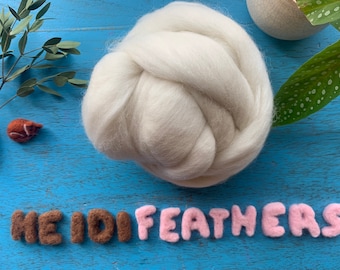 May include: A white ball of wool fiber, with the words "HEIDI FEATHERS" spelled out in brown and pink felt letters.
