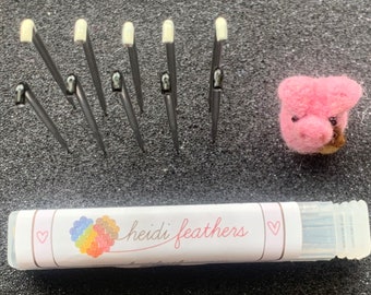 May include: A set of 8 felting needles with white tips, a pink felt pig, and a clear plastic tube with a label that reads "heidi feathers".
