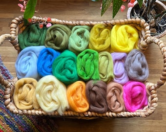May include: A woven basket filled with colorful wool roving in shades of green, blue, yellow, orange, pink, and brown. The basket has two handles and sits on a wooden surface. A houseplant is in the background.
