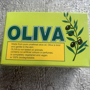 May include: A green and yellow box with the word "OLIVA" in large green letters. The box has a picture of an olive branch with olives. The text on the box reads: "Made from pure unrefined olive oil, Oliva is kind and gentle to the skin. OLIVA is not tested on animals. contains no artificial colours or perfumes. is completely vegetarian and vegan. is 100% biodegradable."