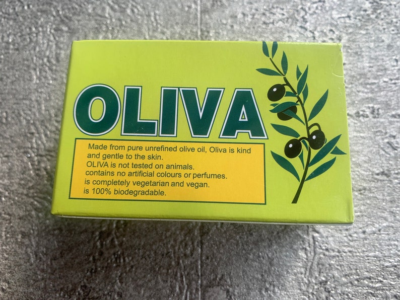 May include: A green and yellow box with the word "OLIVA" in large green letters. The box has a picture of an olive branch with olives. The text on the box reads: "Made from pure unrefined olive oil, Oliva is kind and gentle to the skin. OLIVA is not tested on animals. contains no artificial colours or perfumes. is completely vegetarian and vegan. is 100% biodegradable."