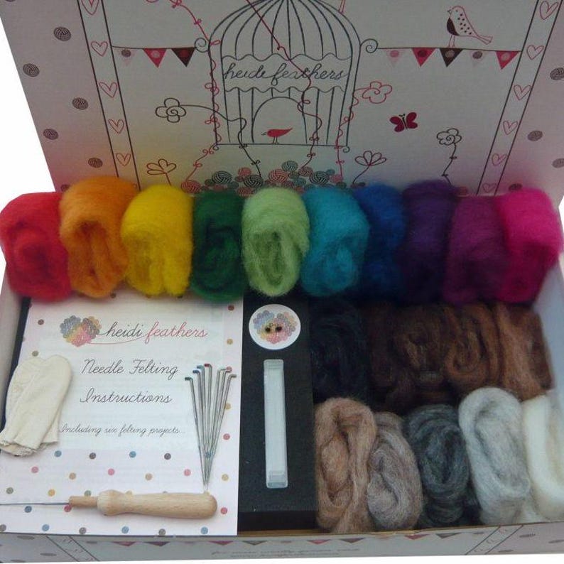 May include: An open box filled with colorful wool roving and needle felting supplies. The box includes a variety of colors, including red, orange, yellow, green, blue, purple, brown, gray, and white. The box also includes felting needles, a foam pad, and a pair of felting gloves. The box is labeled "Heidi Feathers Needle Felting Instructions, Including six felting projects."