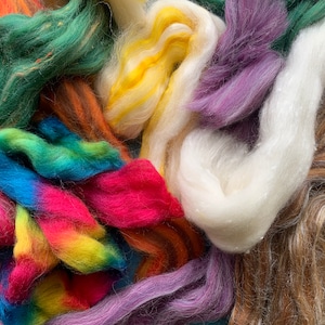 May include: A collection of colourful wool roving in shades of green, yellow, purple, white, orange, pink, blue, and brown. The wool is arranged in a pile, with some strands overlapping.