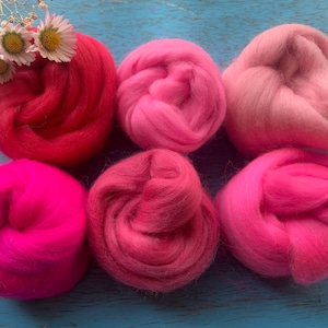 May include: Six balls of wool in various shades of pink and red. The wool is arranged in a gradient from red to pink.