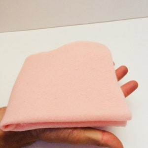 May include: A soft, pale pink felt fabric sheet folded in half. The fabric is smooth and has a slightly fuzzy texture.