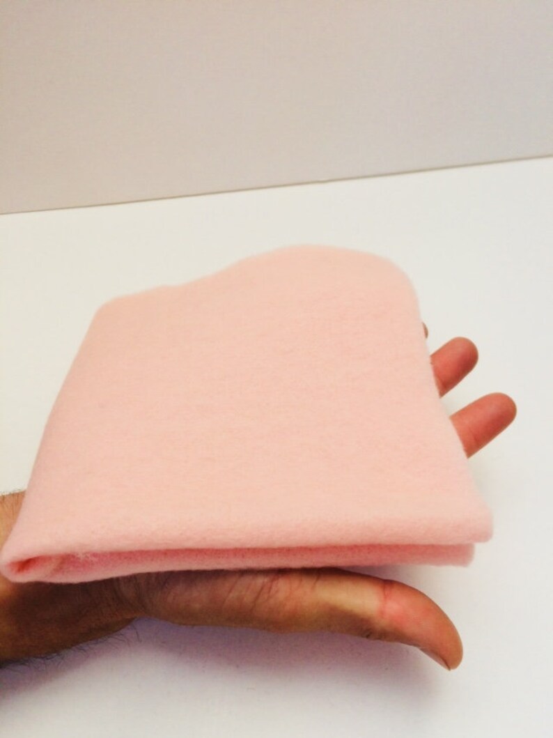 May include: A soft, pale pink felt fabric sheet folded in half. The fabric is smooth and has a slightly fuzzy texture.
