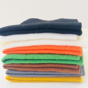 May include: A stack of eight felt squares in various colors, including black, white, orange, green, brown, gray, and yellow.