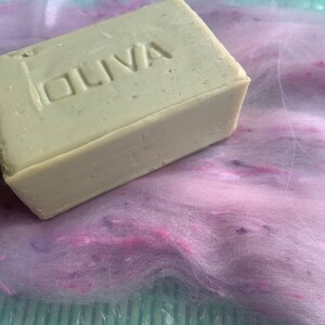May include: A bar of olive oil soap, labelled "OLIVA", on a pink and purple fabric background.