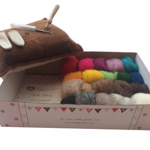 May include: A needle felting kit with a brown felting pad, two felting needles, a needle holder, and a variety of colorful wool fibers in a pink and white box. The box has the text "Needle Felting Instructions" and "for more woolly goodness visit www.heidifeathers.com".
