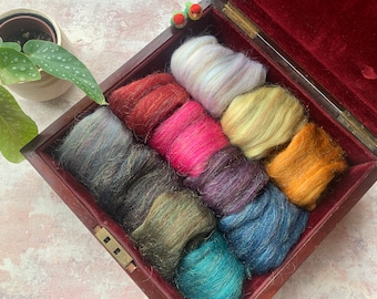 May include: A wooden box filled with colorful wool roving. The roving is arranged in a circle with the colors alternating. The colors are teal, blue, purple, pink, red, yellow, green, and white.