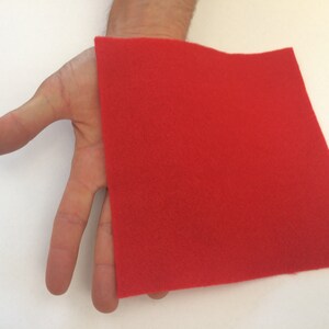 May include: A red felt square, approximately 10 inches by 10 inches, is held in a person's hand.