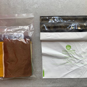May include: A clear plastic bag filled with various colors of felt fabric. Next to it is a white compostable mailing bag with the text "Compostopack This bag is compostable" printed on it.