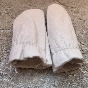 May include: A pair of white leather finger cots, designed to protect fingers while sewing or crafting.