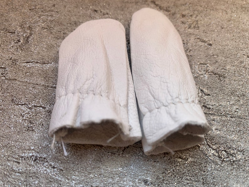 May include: A pair of white leather finger cots, designed to protect fingers while sewing or crafting.