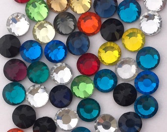 May include: Assortment of colourful round rhinestones in various shades of blue, green, red, yellow, orange, and black. The rhinestones are arranged in a random pattern on a white background.