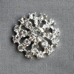 May include: A silver brooch featuring a cluster of clear rhinestones in a circular design.