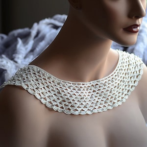 May include: A white crocheted collar with pearl-like beads and rhinestones. The collar is a delicate and intricate piece of jewelry.