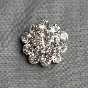 May include: A silver brooch with a cluster of clear rhinestones arranged in a flower shape.