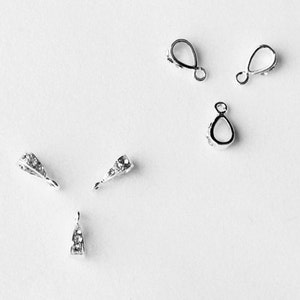 May include: Five silver pendant clasps with clear crystal accents. Two of the clasps are teardrop shaped, and three are rectangular with rounded corners.