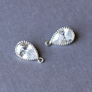 May include: Two silver teardrop-shaped charms with clear crystal stones. Each charm has a small loop for attaching to jewelry.
