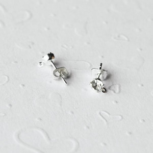 May include: Two silver earring posts with a clear crystal on one post. The posts are designed to hold a charm or bead.