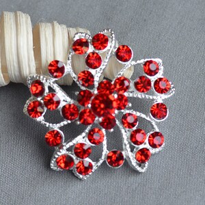 May include: A silver brooch with a red rhinestone flower design. The flower has a swirl pattern and is made up of many small red rhinestones.