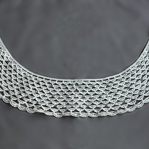 May include: White crocheted lace collar with a scalloped edge.
