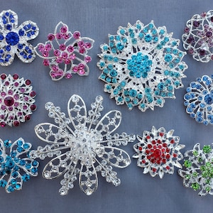 May include: Ten silver brooches featuring a variety of coloured rhinestones. The brooches are shaped like flowers and have a sparkly, ornate design.