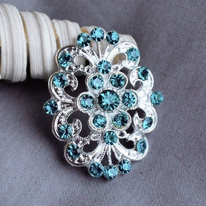 Puede incluir: Un broche de plata con un diseño floral y diamantes de imitación azul turquesa.