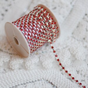 May include: A spool of red rhinestone chain trim. The chain is made of small, square rhinestones connected by silver metal.