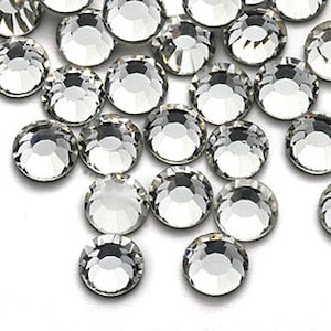 May include: A close-up view of a pile of clear glass rhinestones. The rhinestones are round and have a faceted surface.