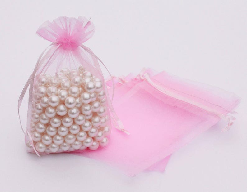 May include: Pink organza gift bags with a drawstring closure. The bags are filled with white pearl beads.
