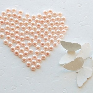 May include: A heart shape made of pink pearl beads with white paper butterflies on a white background.