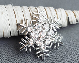 Könnte beinhalten: Eine silberne Schneeflockenbrosche mit klaren Strasssteinen. Die Schneeflocke ist eine beliebte Weihnachtsdekoration.
