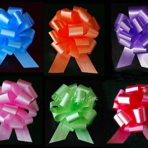 Może przedstawiać: Sześć dużych, gotowych kokard do prezentów w różnych kolorach. Kokardy są wykonane z satynowej wstążki i idealnie nadają się do dodania elegancji każdemu prezentowi.