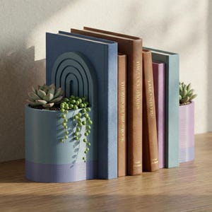 May include: A decorative bookend with a built-in planter, holding a succulent and trailing plant. The bookend is blue and purple, with a curved arch design. Several books in various colors stand next to the bookend on a wooden surface.