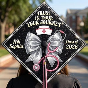 May include: A black graduation cap decorated with a silver bow, rhinestones, and a pink stethoscope. The cap has the text "Trust in Your Journey", "RN Sophia", and "Class of 2026". A nurse's hat with a red cross is also featured.